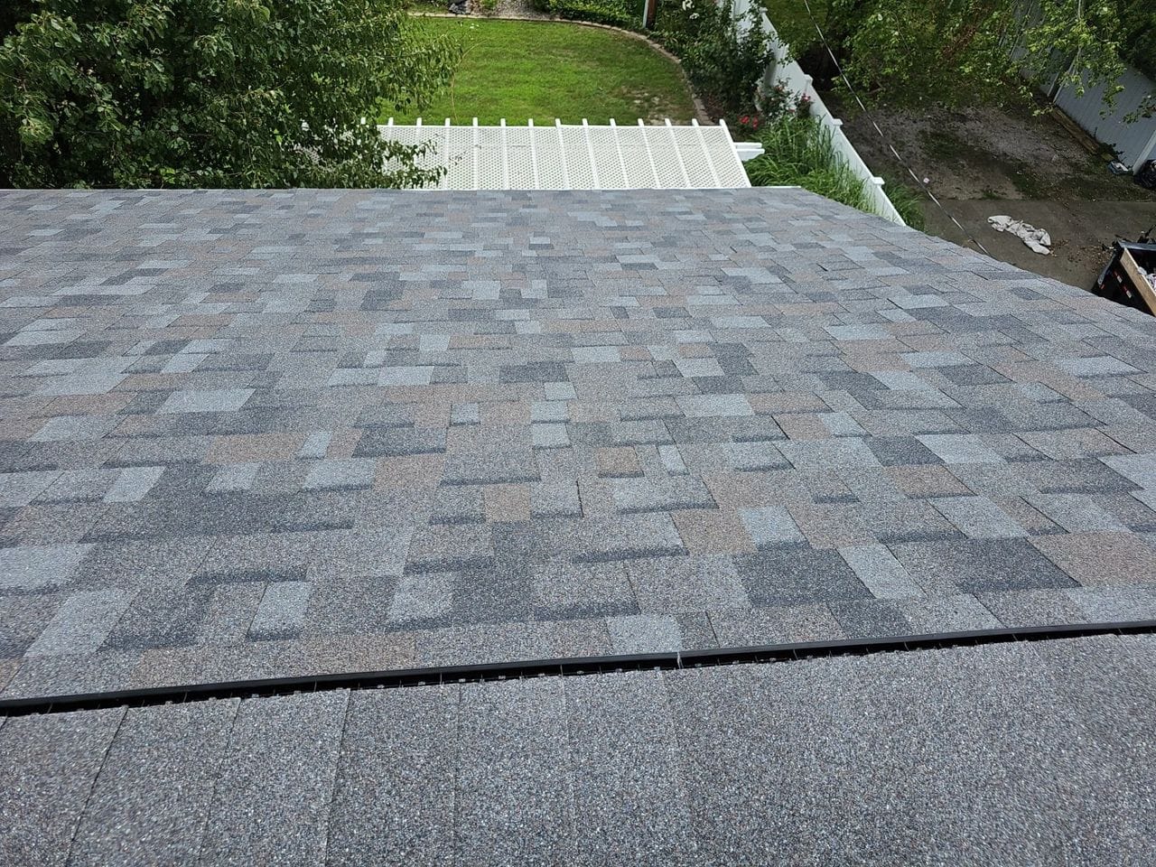 Newly installed multi-tone architectural asphalt shingles with a ridge vent, seen from the peak over a backyard
