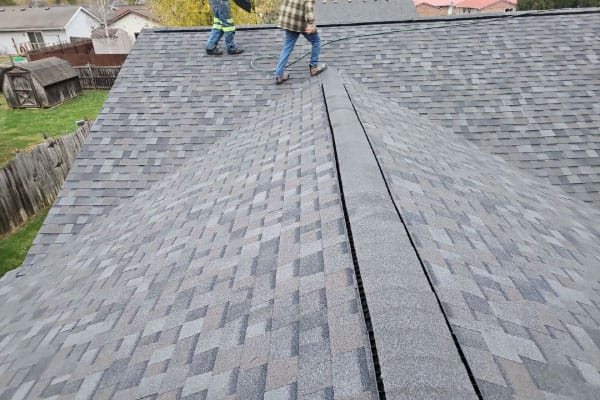 Two roofers walking the peak of a new gray architectural shingle roof with a ridge vent