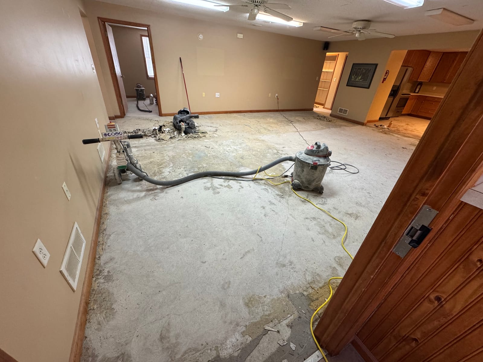 Office space with carpet removed, bare concrete with adhesive residue, a floor scraper and a shop vac