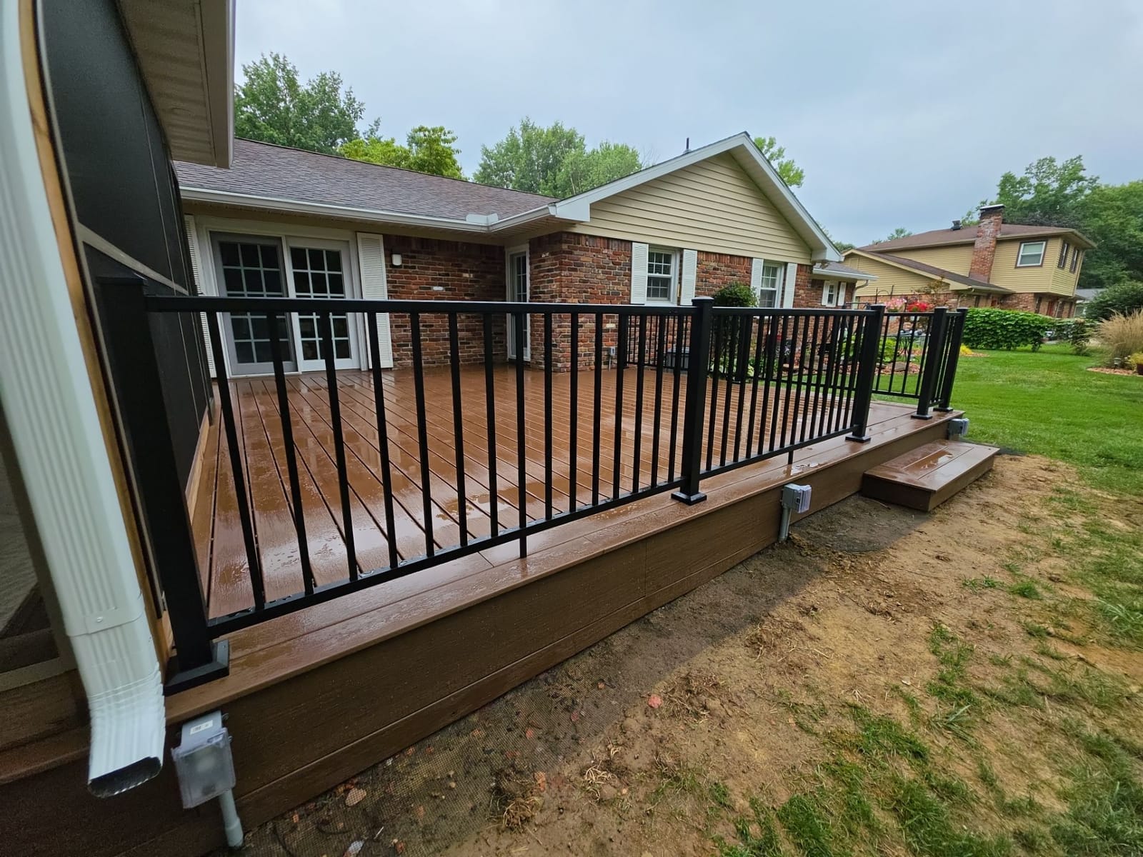 Brown composite deck with black aluminum railing, box step and composite fascia along a brick ranch house