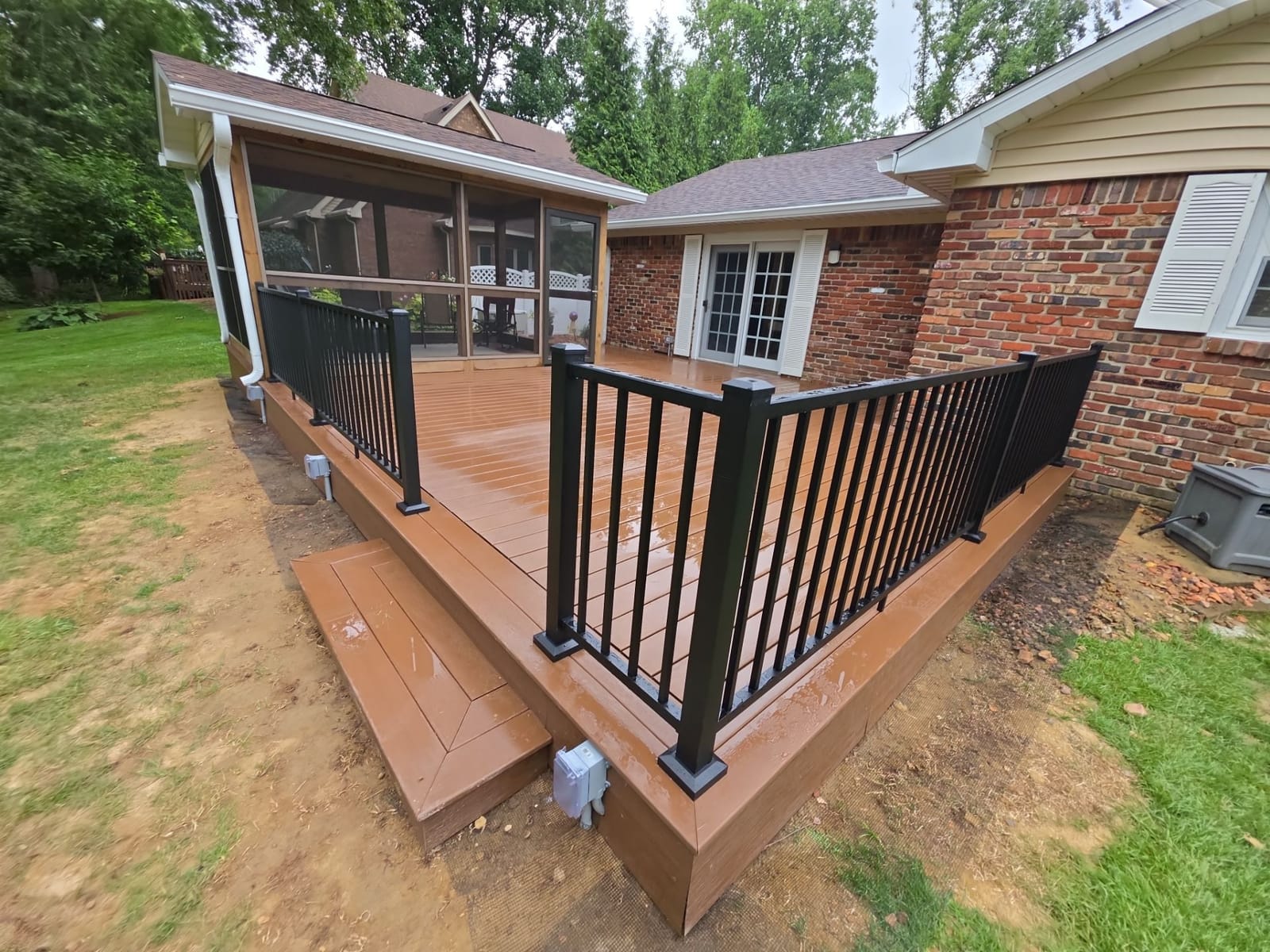 Brown composite deck with black aluminum railing and steps, attached screened porch with gable roof, brick ranch house
