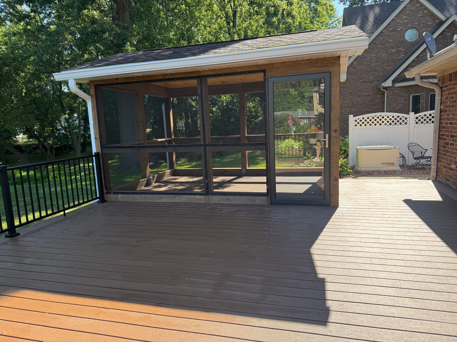 Brown composite deck with black aluminum railing leading to a screened porch with a glass storm door