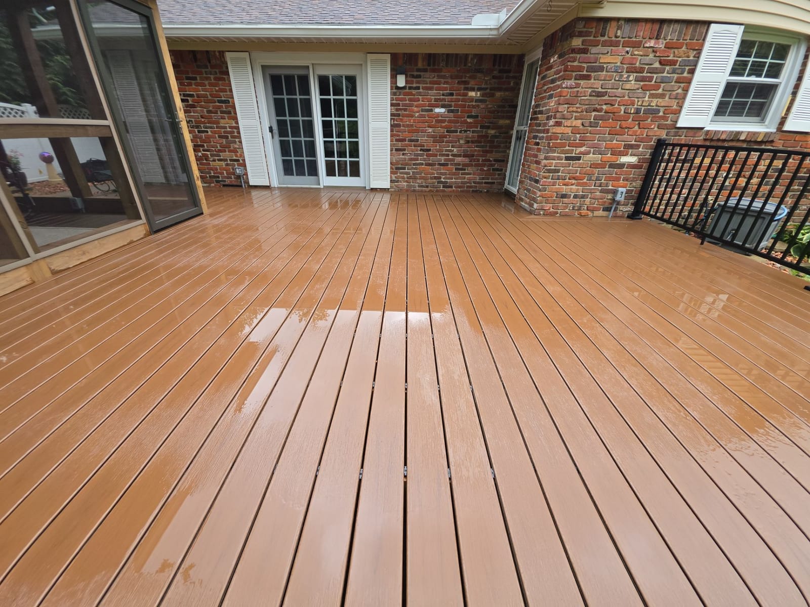 Brown composite deck along a brick house with French doors, a screened porch at left and black aluminum railing