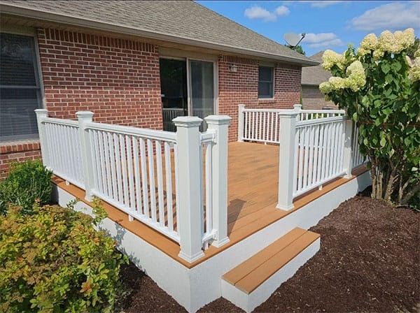 Composite deck with white vinyl railing, white skirting and a box step, next to a brick home and hydrangea