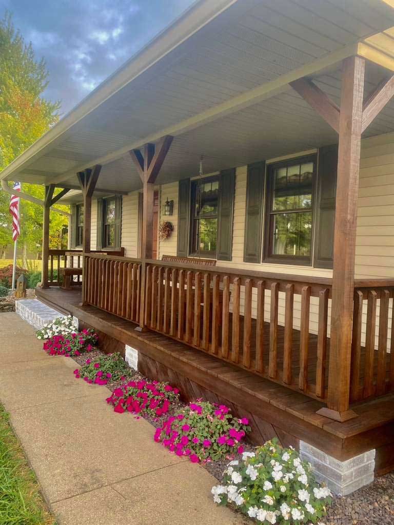 Covered front porch with stained wood posts, knee braces and spindle railing, wood floor and a flower bed along the walk