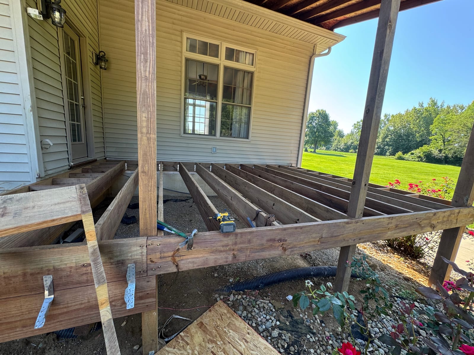 New pressure-treated joists with hangers framing a covered front porch floor beside tan vinyl siding
