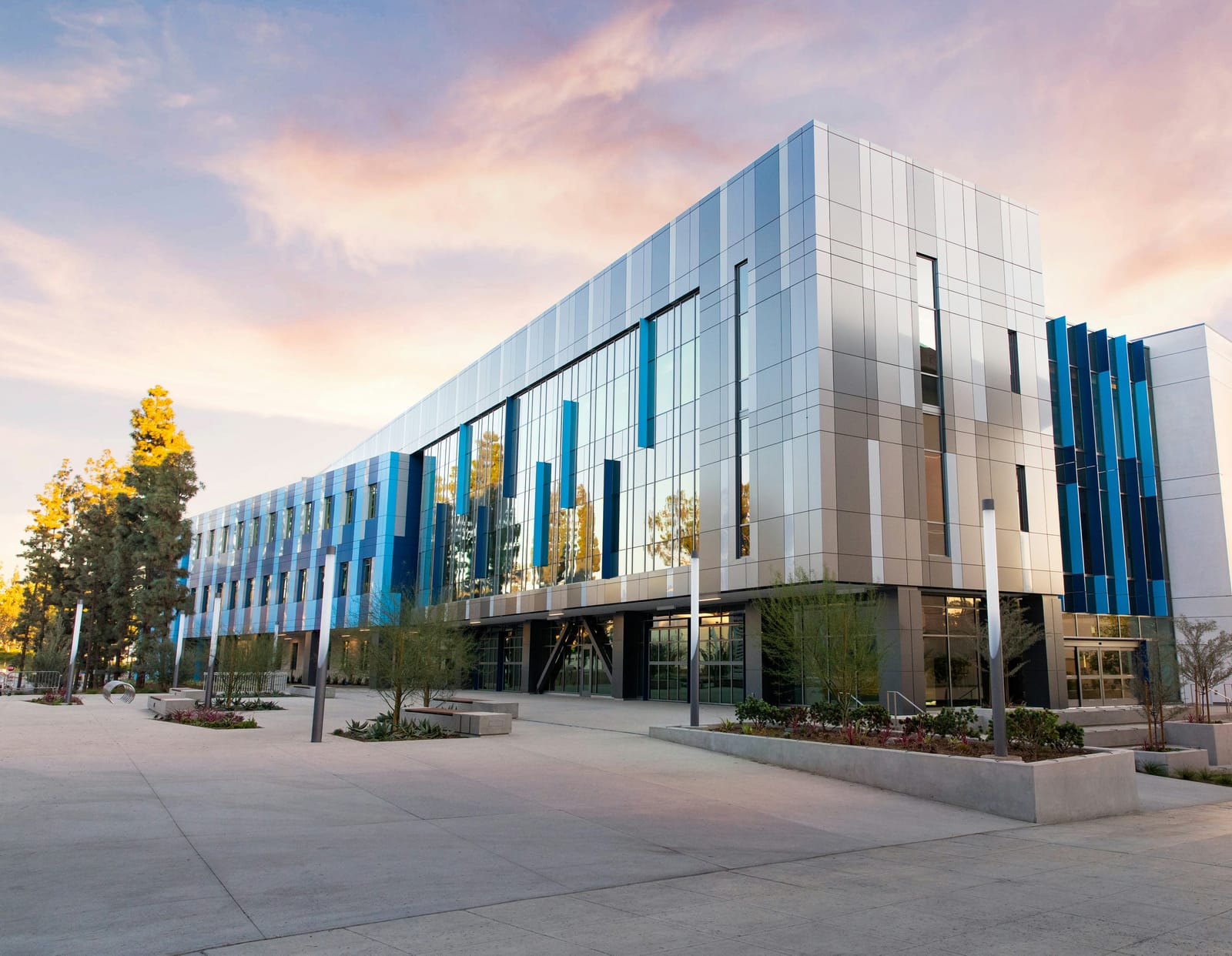 Example of modern three-story commercial building with metal panels and a glass curtain wall under a pink sunset sky (stock photo)
