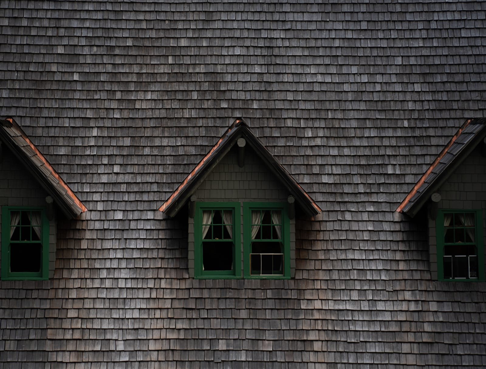 Example of weathered gray shake roof with three gabled dormers and green-trimmed windows (stock photo)