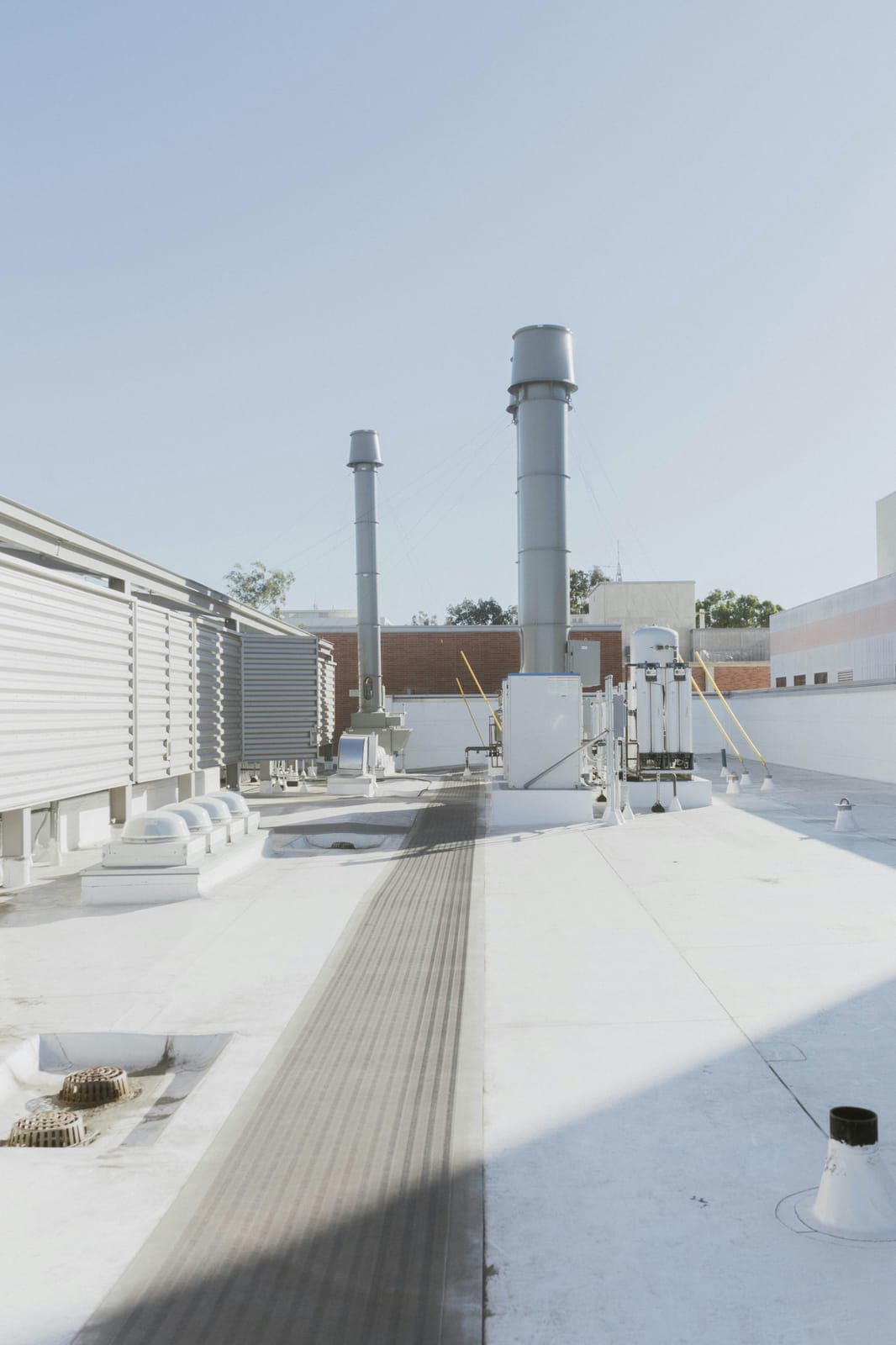 Example of white single-ply membrane roof with a gray walkway pad, roof drains and exhaust stacks on a commercial building (stock photo)