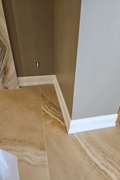 Large-format onyx-look porcelain tile floor meeting white baseboard at a wall corner