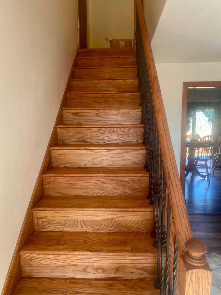 Straight staircase with oak treads and risers, wrought iron balusters and an oak handrail and newel post
