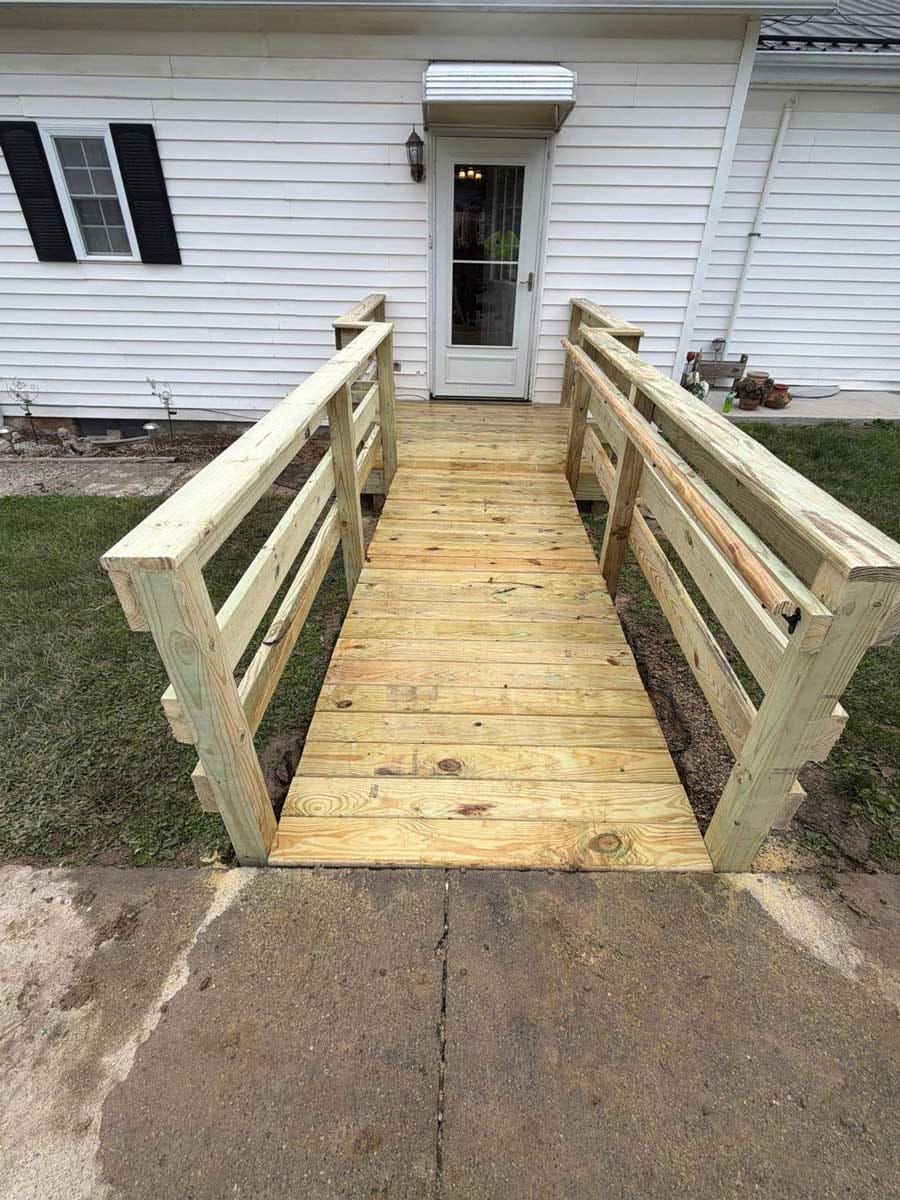 Pressure-treated wood access ramp with double handrails leading to the back door of a white-sided house