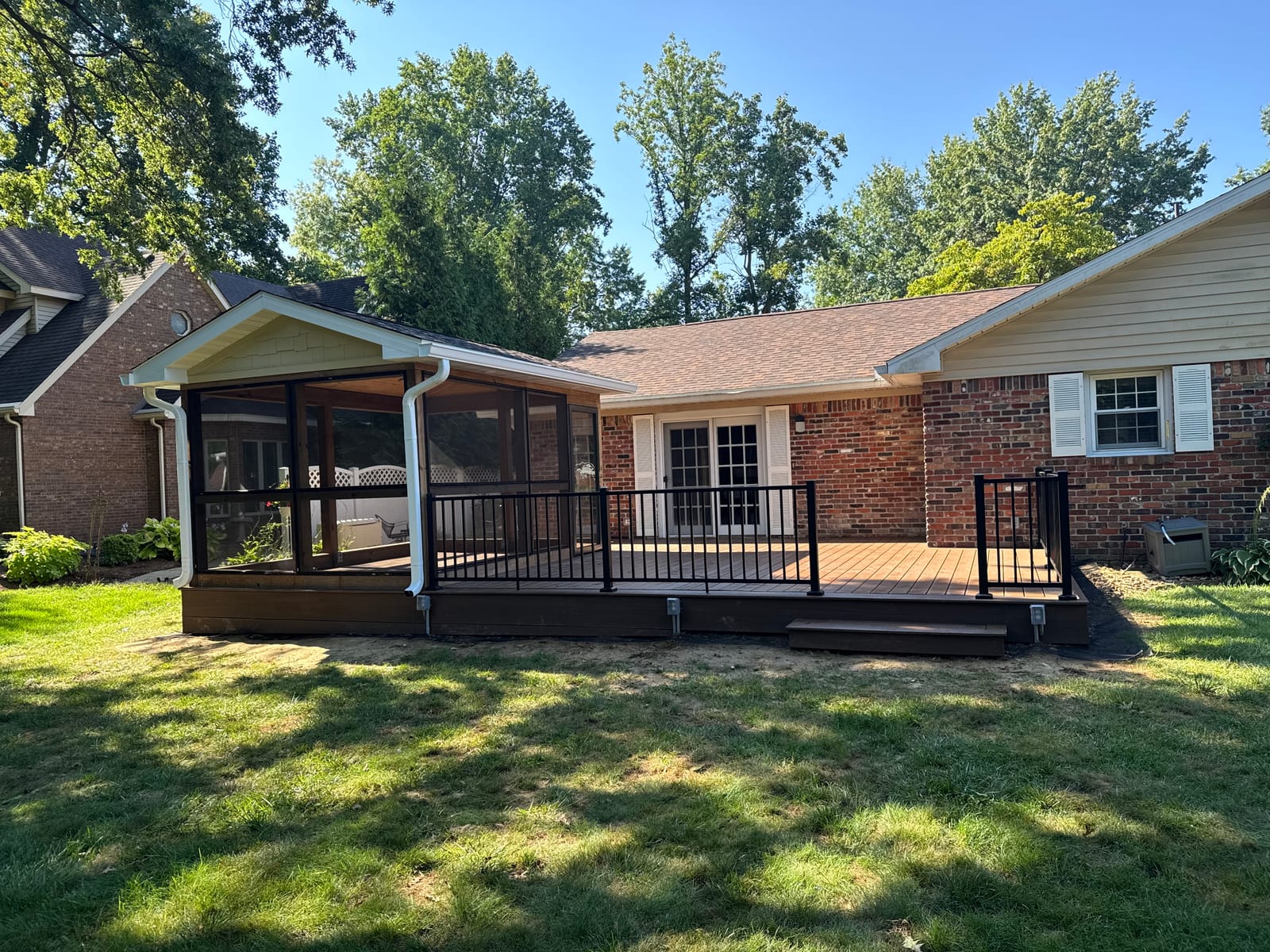 Brick ranch with a new screened porch and brown composite deck with black aluminum railing over a lawn