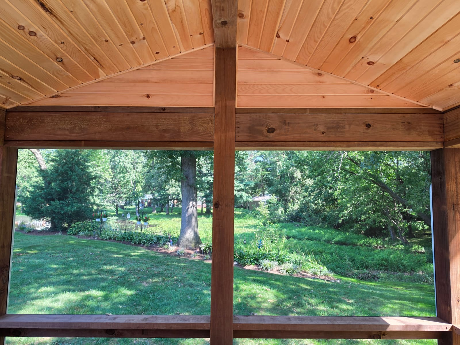 View from a screened porch framed by stained posts and beam under a tongue-and-groove pine ceiling, lawn beyond