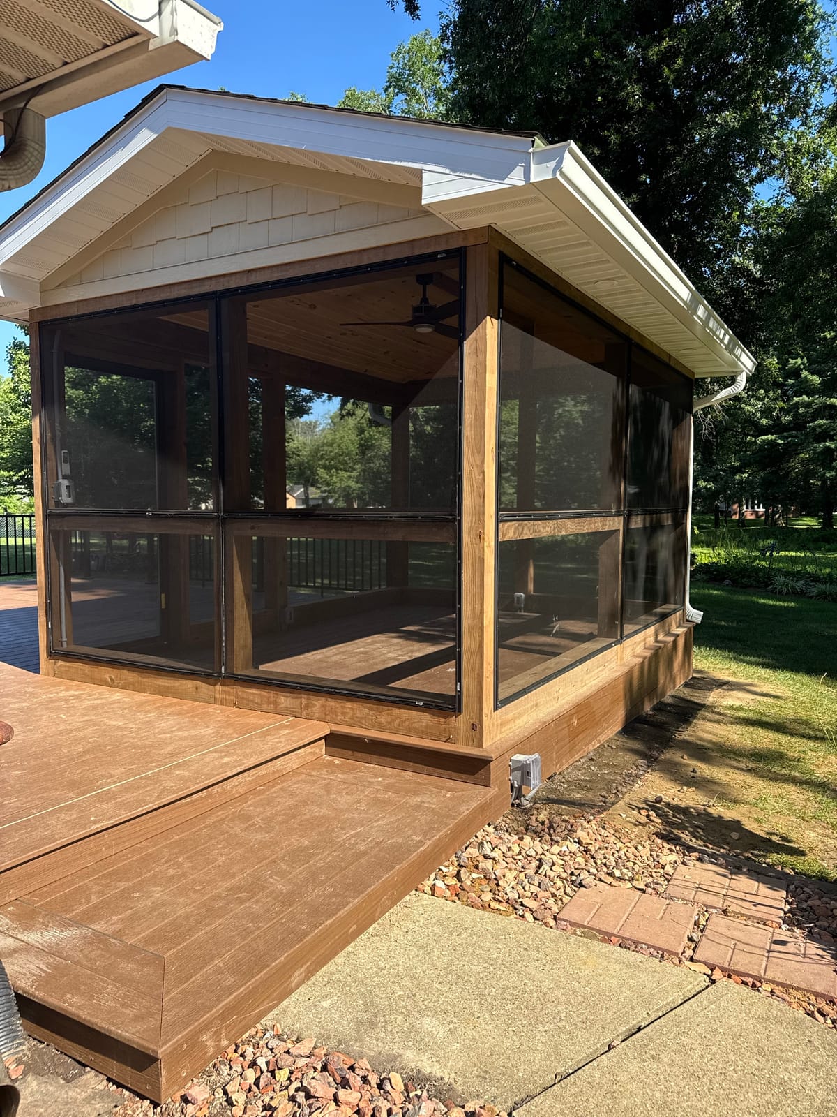 Corner of a screened porch with a shake-siding gable, white gutters and composite steps down to a walkway