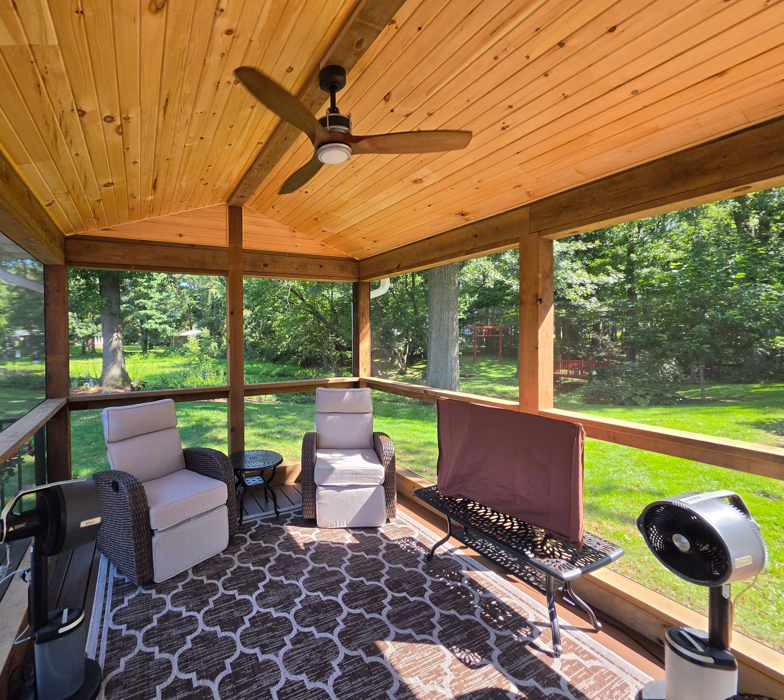 Screened porch with knotty pine vaulted ceiling, ceiling fan and wicker recliners overlooking a wooded backyard