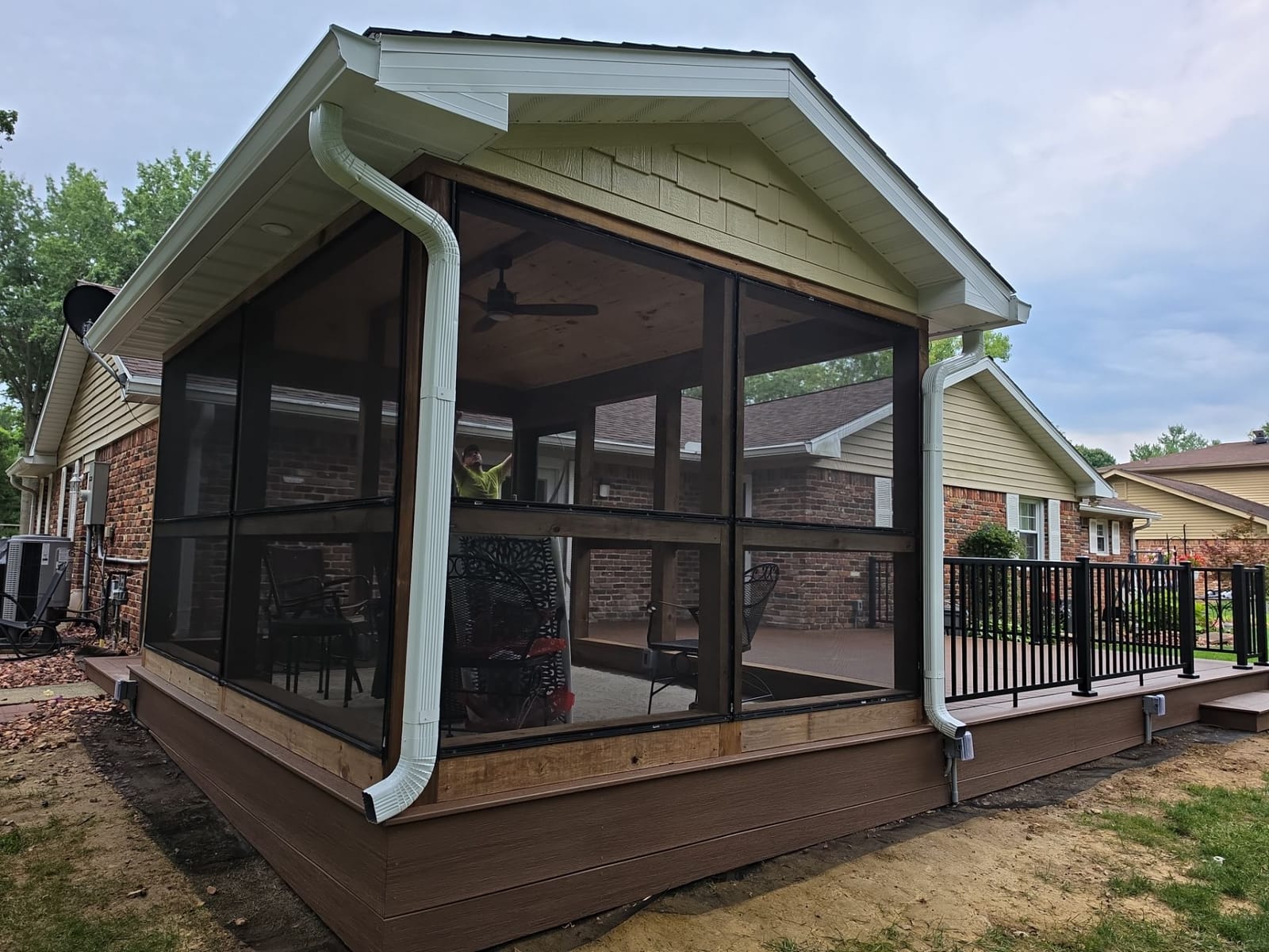 Screened sunroom with shake-style gable and white gutters on a composite deck with black aluminum railing