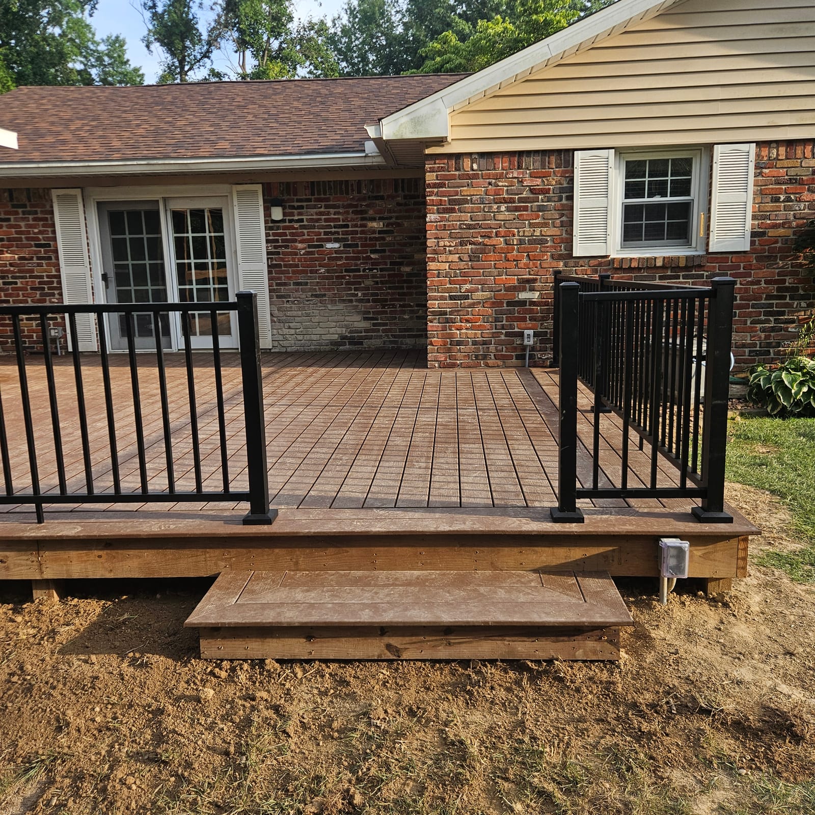 Brown composite deck with picture-frame border, black aluminum railing and a box step against a brick house