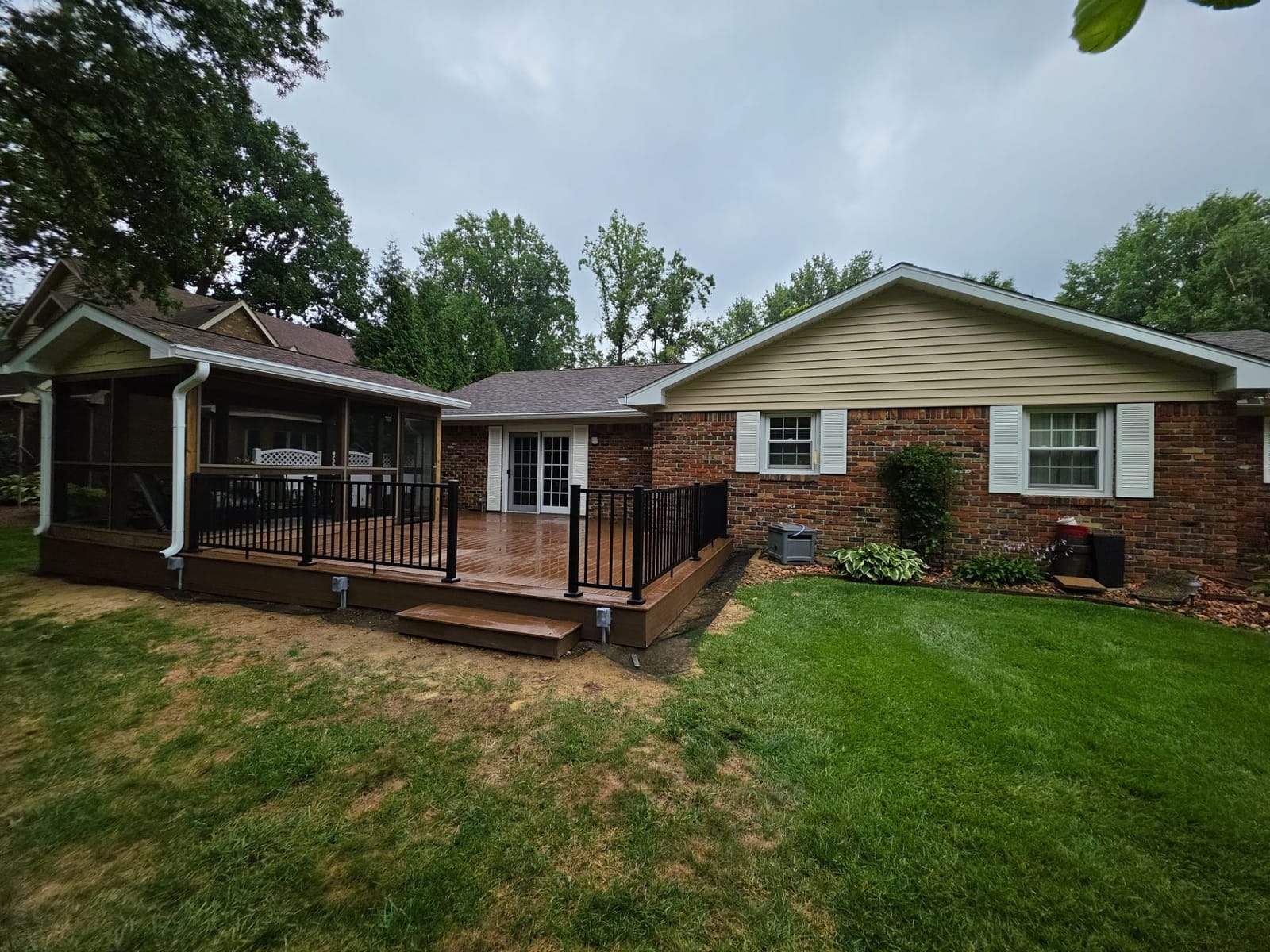 Brick ranch with a new brown composite deck, black aluminum railing, box step and a gable-roof screened sunroom