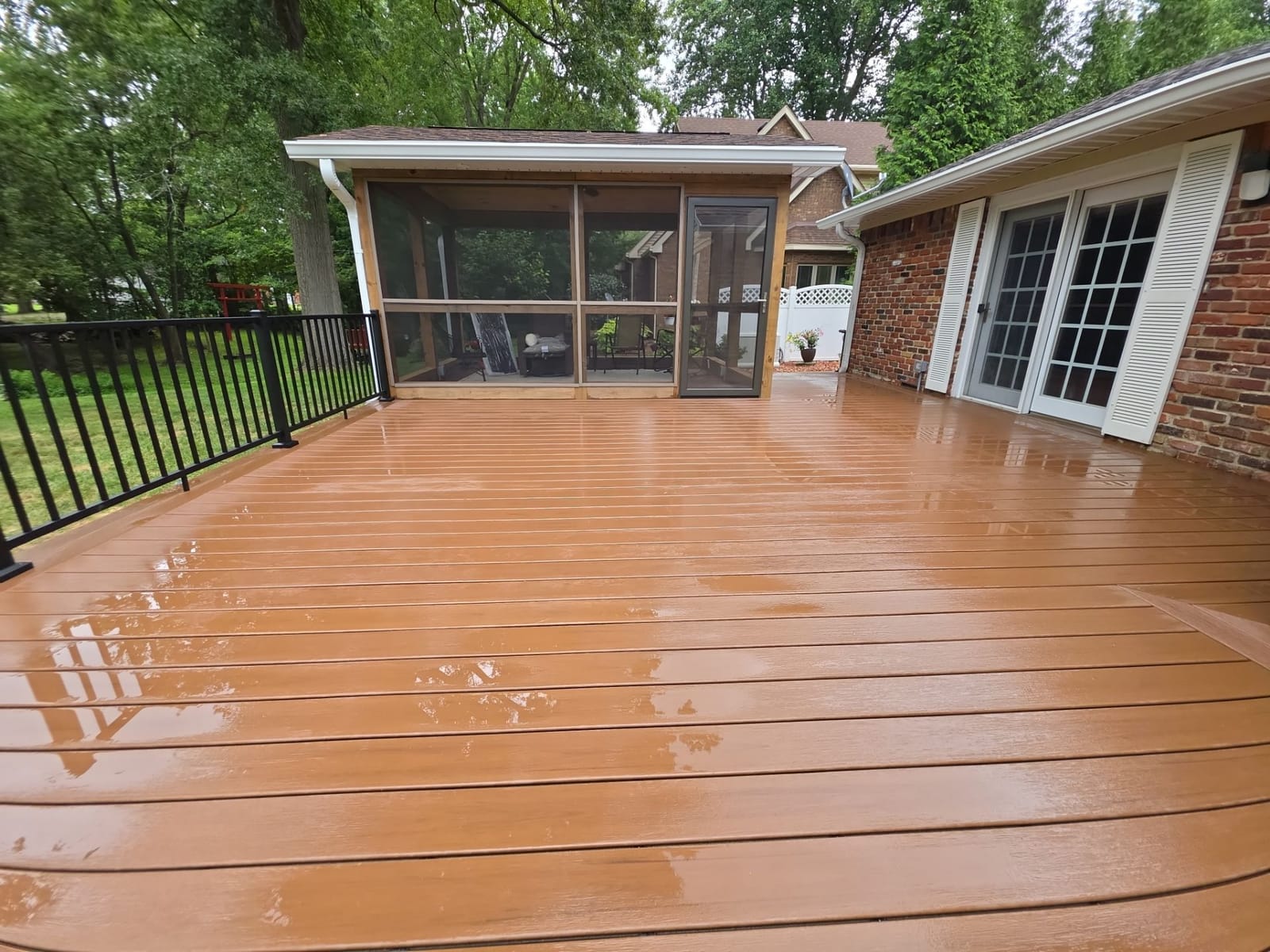 Wide brown composite deck with black aluminum railing leading to a screened sunroom and French doors