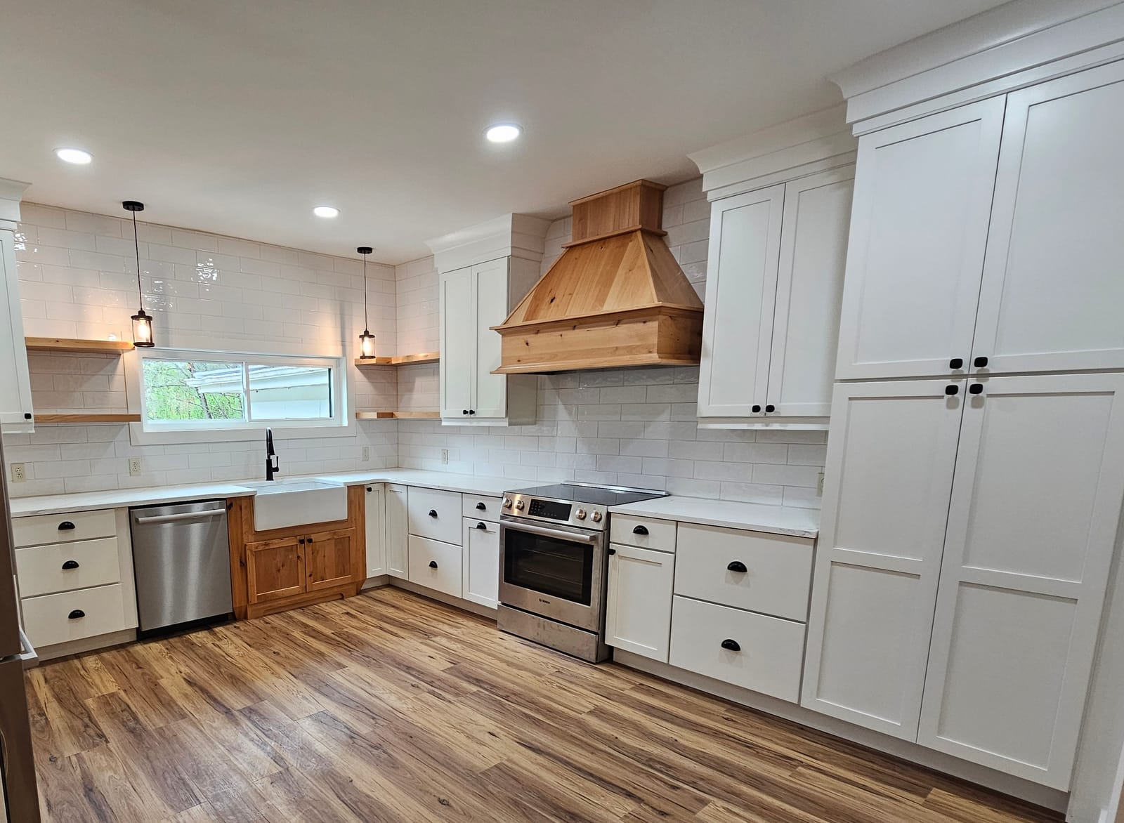 White shaker kitchen with natural knotty-wood range hood, subway tile, farmhouse sink and wood-look plank floor