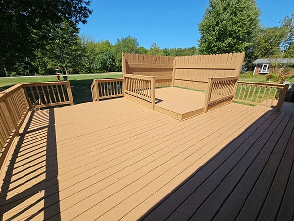 Wood deck in tan solid stain with a privacy screen wall and raised corner platform with railings