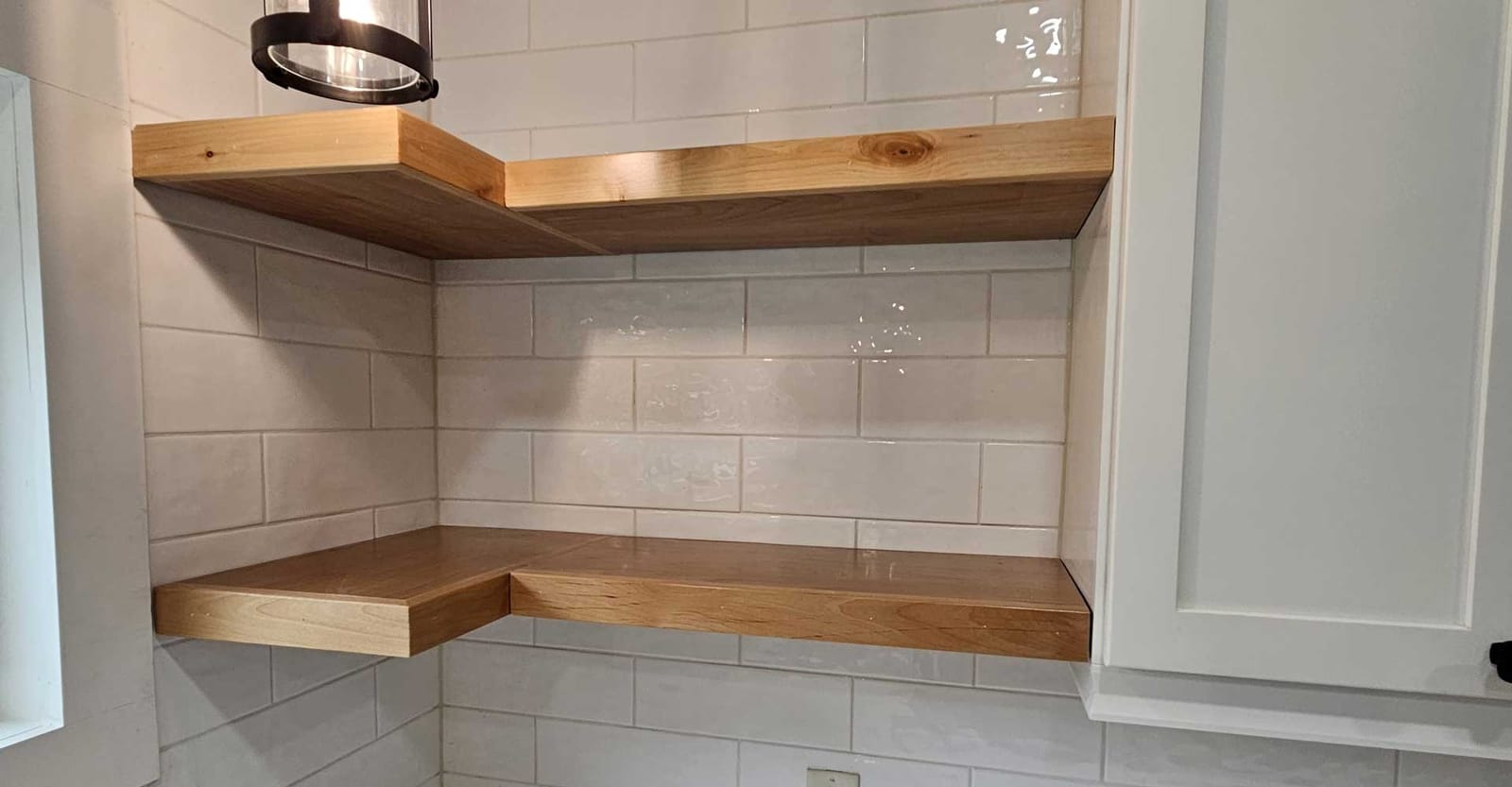 Natural wood floating corner shelves on white handmade-look subway tile beside a white shaker cabinet